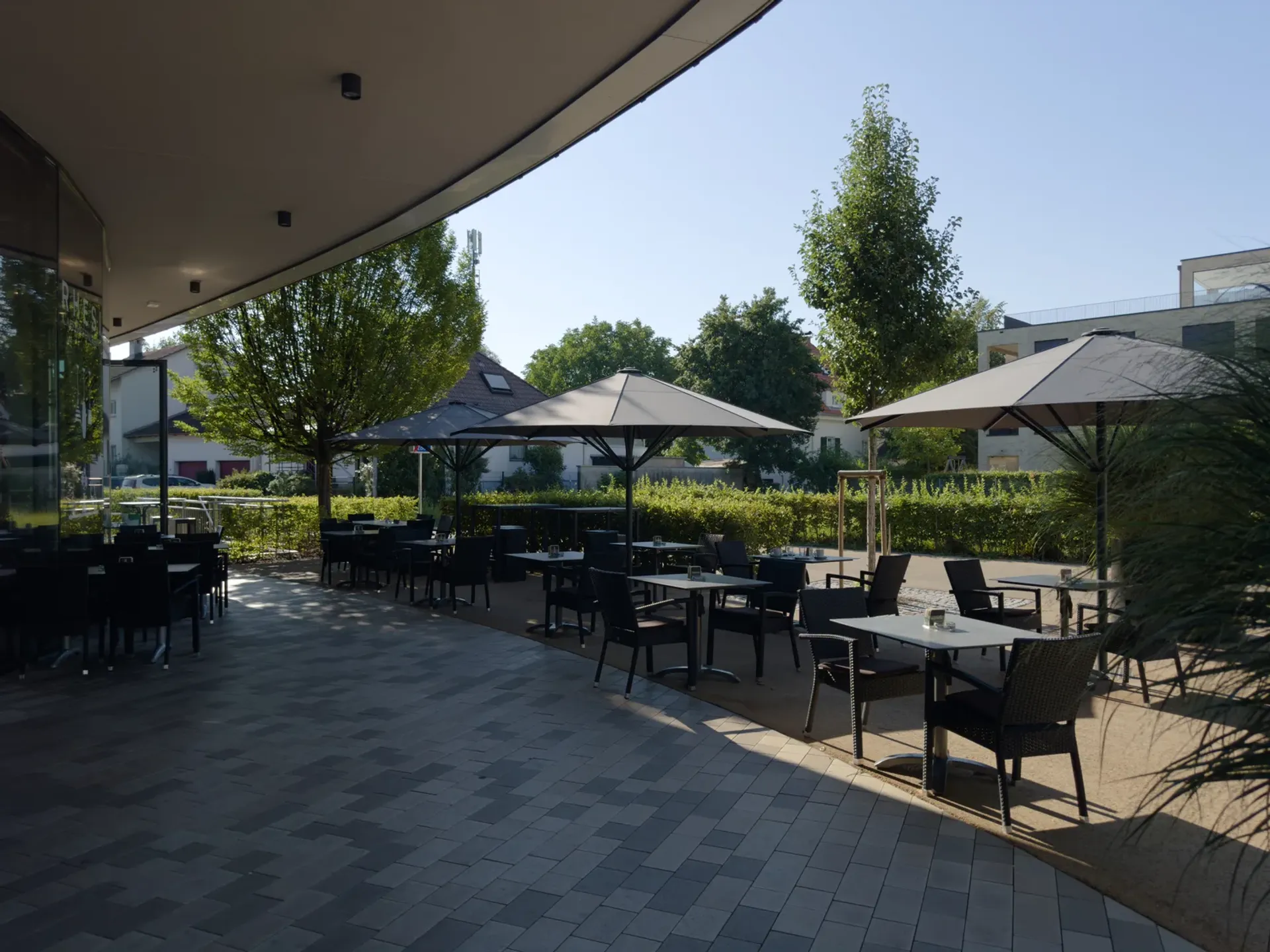 Sonniger Gastgarten des Rhesi Café & Restaurant mit Tischen und Sonnenschirmen